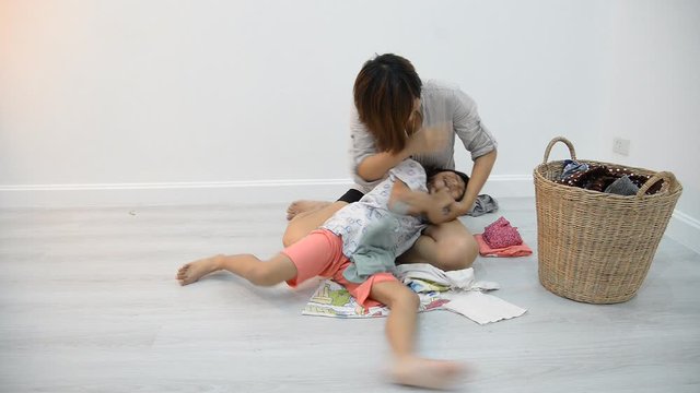 Slow motion mother tickling her daughter on floor during fold clothes at home