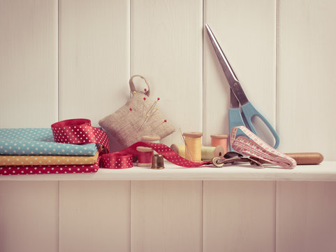 Set of tools for sewing and fabric lying on the wooden shelf.