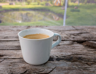 Cup of coffee on wooden surface near the garden pond