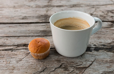 Cup of coffee and cupcake on a dark wooden surface.
