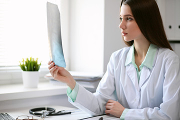 Female doctor brunette sitting  at the table near the window in hospital and typing at laptop computer