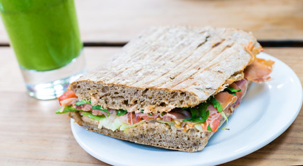 Sandwich serviert with smoothie on wooden table.