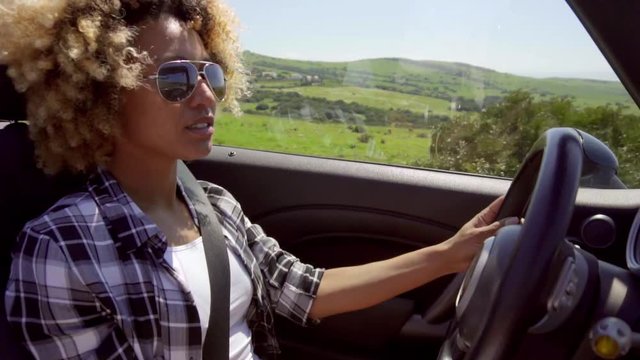 Young woman in sunglasses driving her car through a scenic landscape viewed through the drivers window