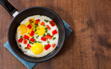 fried eggs with vegetables in a frying pan on wooden table