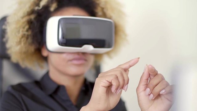 Young african-american businesswoman wearing 3d vr goggles working in virtual reality by using her hands and fingers against virtual objects.