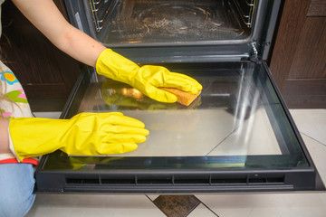 housework and housekeeping concept - close up of woman hands in gloves. Cleaning oven door,