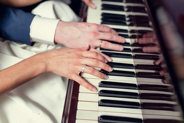 Hands of newlyweds with wedding rings on piano