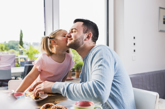 Daughter kissing father at breakfast table