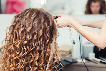 Hairdresser curling woman hair with electric iron curler tong. Hairstylist making girl hairstyle.