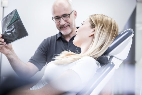 Dentist showing x-ray image to patient, sitting in dentist's chair