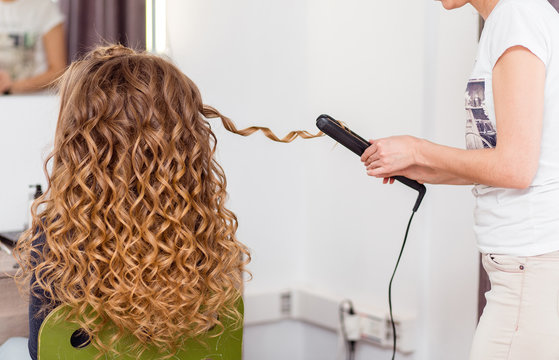Hairdresser curling woman hair with electric iron curler tong. Hairstylist making girl hairstyle.