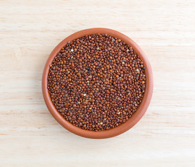 Red quinoa in a small bowl on a wood table top view