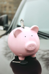 Piggy money box with cash and key on car bonnet at the street