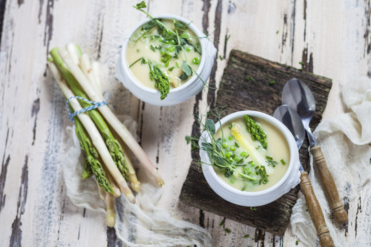 Cream of white asparagus soup garnished with white and green asparagus spears, pea shots and chives