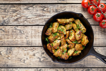 Fried sliced chicken or turkey fillet meat with chopped parsley and tomatoes on rustic wooden table background