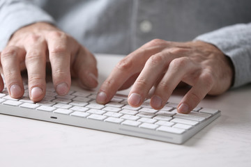 Male hands typing on wireless keyboard at table closeup