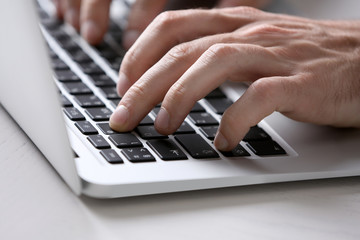 Male hands typing on laptop keyboard at table closeup