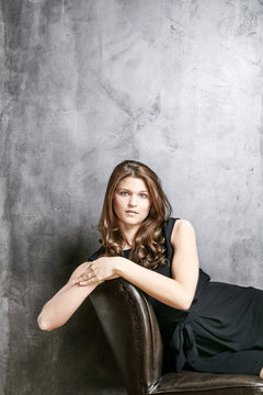 Portrait of young woman wearing black dress on leather chair