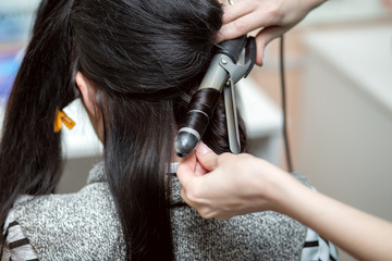 Fototapeta premium The Barber makes an Evening or wedding hairstyle with long beautiful dark hair in hairdresser salon