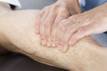 Closeup of hands of chiropractor doing calf muscle massage to ma