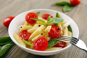 Plate of pasta with cherry tomatoes and basil leaves on table closeup