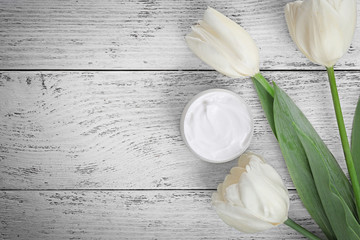 Cosmetic cream with tulips on white wooden background