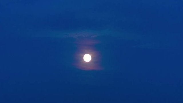 time lapse of the full moon passing through the moving evening clouds in the blue sky getting gradually dark
