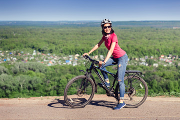 Fototapeta na wymiar Pretty young woman on the bike at the top of the hill
