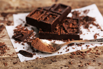 Spoon with cocoa powder and chocolate bar pieces  on wooden background