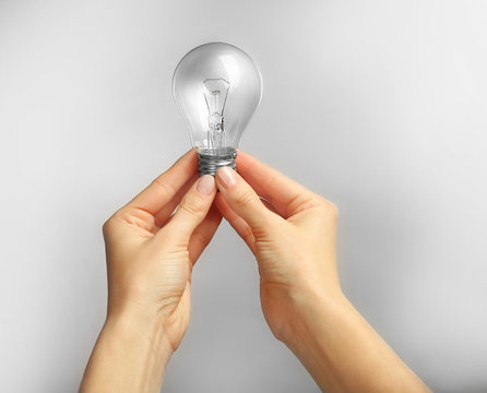 Woman hands holding bulb on grey background