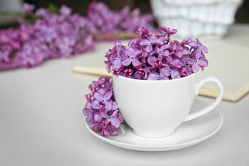 Purple lilac flowers and cup on white table