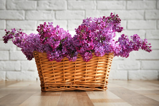 Purple lilac flowers in a basket on white brick wall background