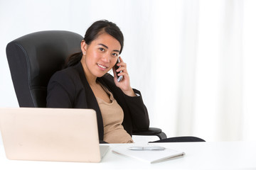Beautiful asian businesswoman sitting at desk and talking at phone