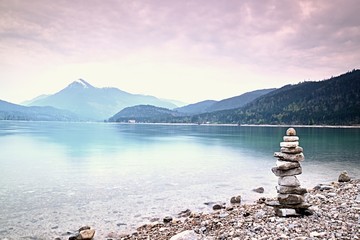 Balanced stone pyramide on shore, blue water of mountain lake.