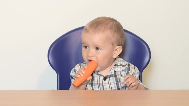 Baby child sits at a table and eats a carrot.