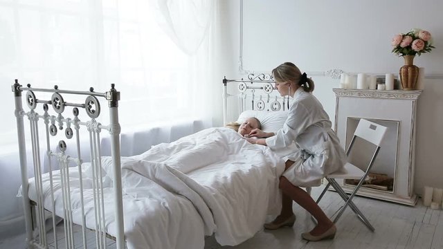 Woman doctor with a stethoscope auscultating to the child lying in the bed.Doctor or nurse examines the girl in the bed stethoscope.The doctor in a white room with a stethoscope.Woman doctor with a