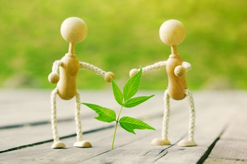Two wooden little men surround green leaf. Concept of growth, ec