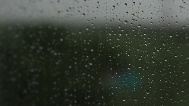 Close up image of rain drops falling on a window with sound of rain and wind