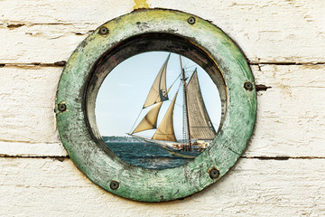 Old porthole window looks out at an old sailing ship. Vintage color