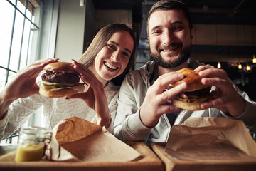 A woman and a man are enjoying their burgers - obrazy, fototapety, plakaty