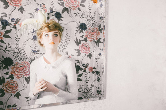 Mirror image of woman in front of floral wallpaper with bird hair ornament