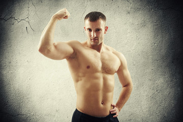Obraz premium Man showing biceps on right arm over concrete wall