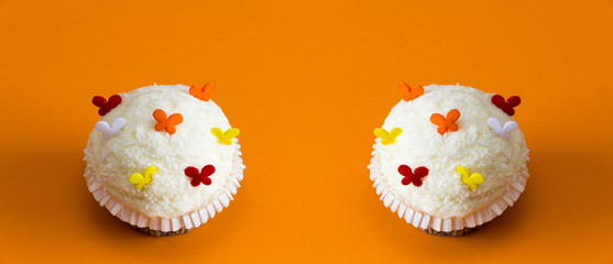 weiße cupcakes auf orangem Hintergrund und bunter Dekoration Panorama