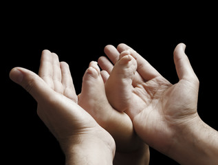 Newborn feet inside a his dad or mom hand isolated on black background