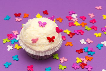 weißer Cupcake mit Kokosnuss und bunten Schmetterlingen auf violettem Hintergrund