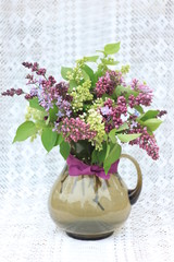 Букет сирени в коричневом стеклянном кувшине на кружевной скатерти