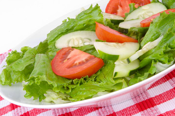 Healthy Salad with Tomatoes and Cucumbers – A plate of fresh lettuce, tomatoes and cucumbers. Red checkered placemat in background.