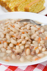Hearty Navy Bean Soup – A bowl of navy bean soup. Cornbread in background.