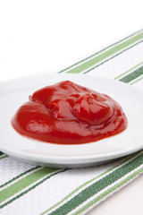 Ketchup on a White Plate – A mound of ketchup on a white plate. Green striped background.