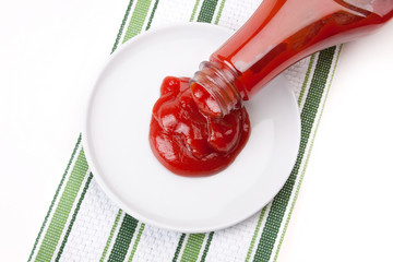 Ketchup Pouring from Bottle – Red ketchup pours from a bottle onto a white plate. Green striped...